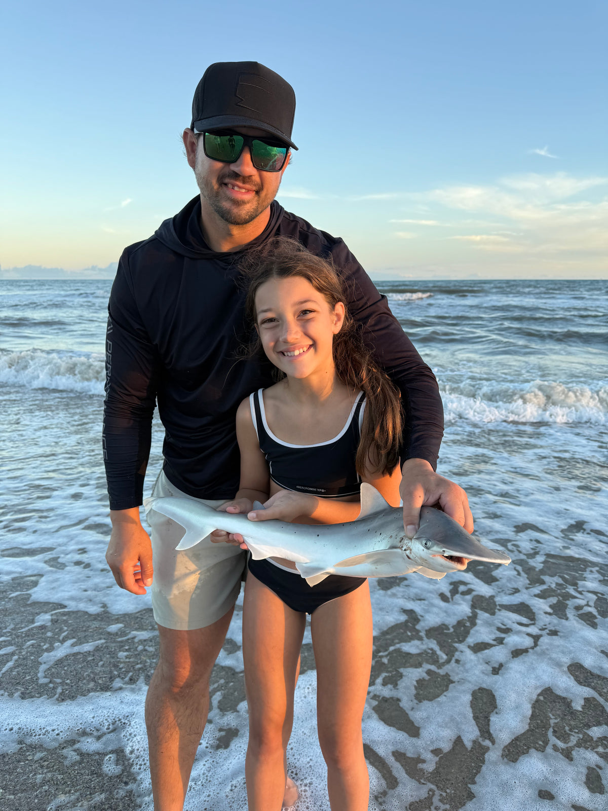 Two people holding a shark on a beach with ocean waves in the background